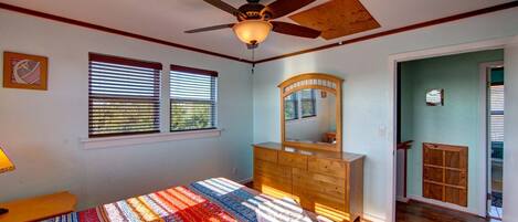 A bedroom with a wooden dresser, a ceiling fan, and a bed with a colorful blanket.