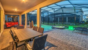 Eine überdachte Terrasse mit Tisch und Stühlen, einem roten Sofa und einem Poolbereich.