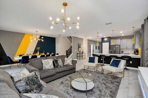 A modern living room with a grey sofa, patterned cushions, a round coffee table, and a chandelier.