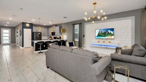Ein modernes Wohnzimmer mit grauem Sofa, einem an der Wand montierten Fernseher und einer Küchenzeile mit grauen Schränken und einer zentralen Kochinsel.