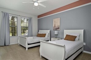 Ein Schlafzimmer mit zwei Einzelbetten, einem Deckenventilator, einem Nachttisch mit Lampe und einem Fenster mit Vorhängen.