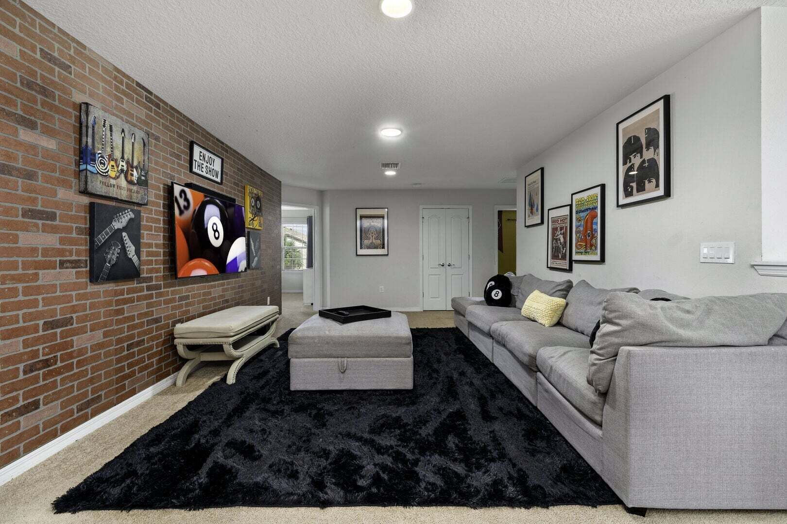 A living room with a brick accent wall, a grey sofa, a black furry rug, and various framed pictures.