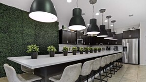 A modern kitchen with a central island, bar stools, pendant lighting, and a green wall.