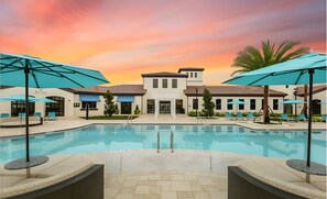 Ein Poolbereich mit Liegestühlen und Sonnenschirmen, ein Gebäude mit einem Ziegeldach und ein Sonnenuntergangshimmel.