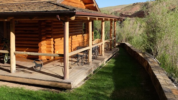 A log cabin with a stone chimney, a covered porch, and a grassy yard.