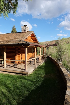 A log cabin with a stone chimney, a covered porch, and a grassy yard.