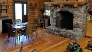 A rustic cabin interior with a stone fireplace, wooden dining table, and chairs.