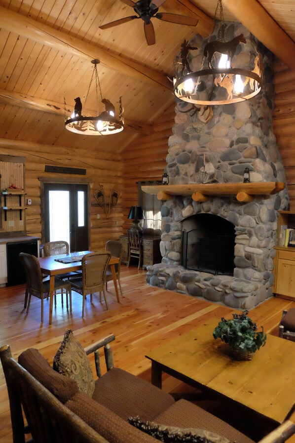 A rustic cabin interior with a stone fireplace, wooden dining table, and chairs.