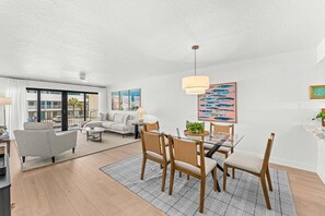 A modern living room with a glass dining table, a sofa, and a large window.