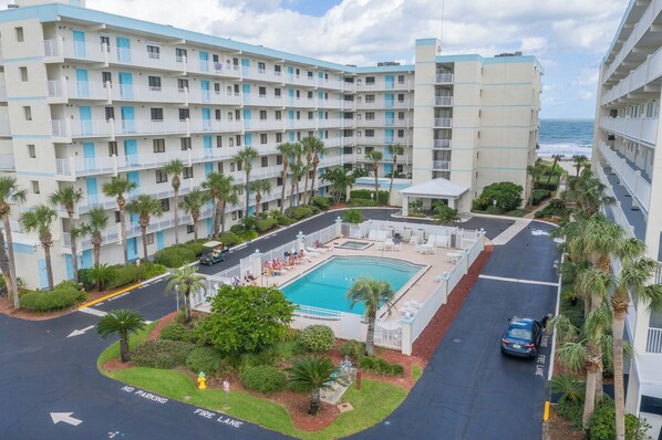 A multi-story hotel with a swimming pool, palm trees, and a view of the ocean.
