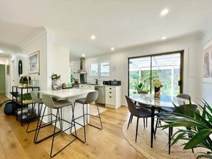Une cuisine moderne avec des meubles blancs, un îlot central, des tabourets de bar et une table à manger avec des chaises.