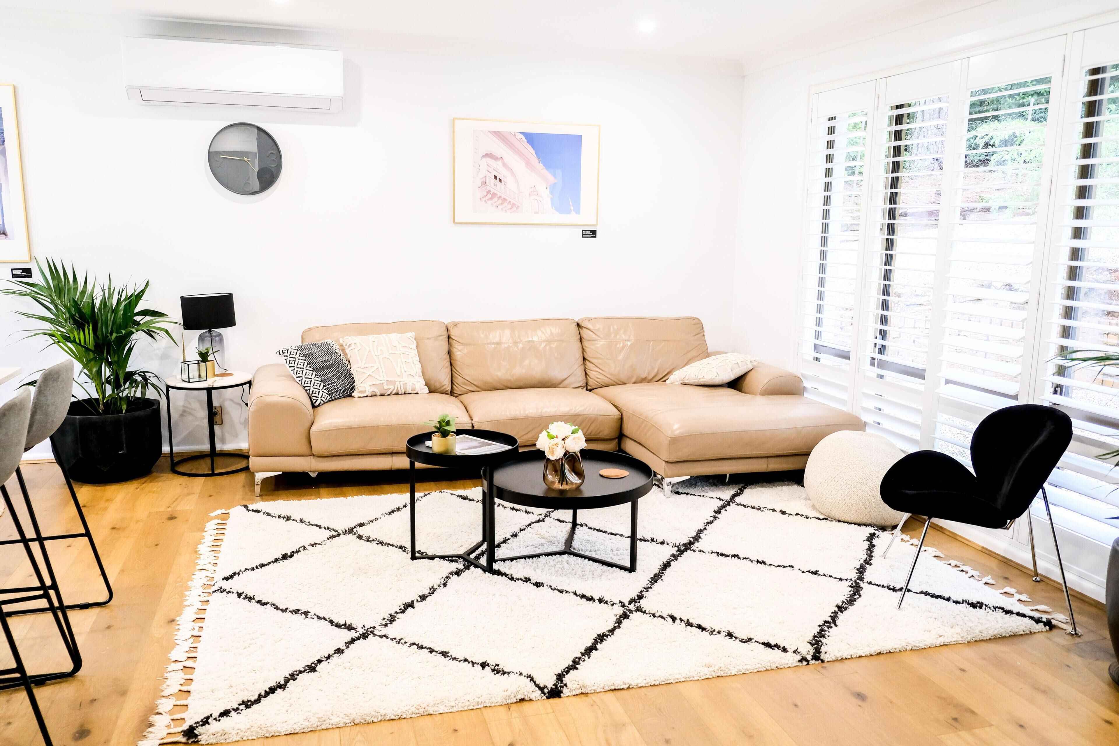 A modern living room with a beige sofa, a black coffee table, and a white rug with black patterns.