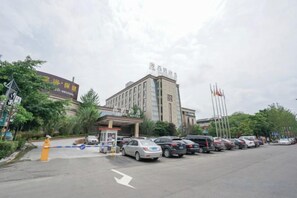 A hotel entrance with a parking lot, a fire hydrant, and a building with flags. - Garden Hotel (Yilong)