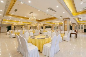 A banquet hall with round tables, white chairs, chandeliers, and a polished floor. - Garden Hotel (Yilong)