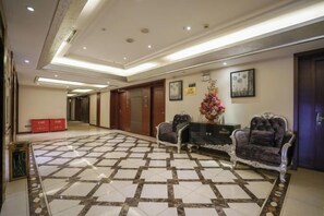A hotel lobby with a patterned floor, a reception desk, a sofa, and a wall-mounted clock. - Garden Hotel (Yilong)