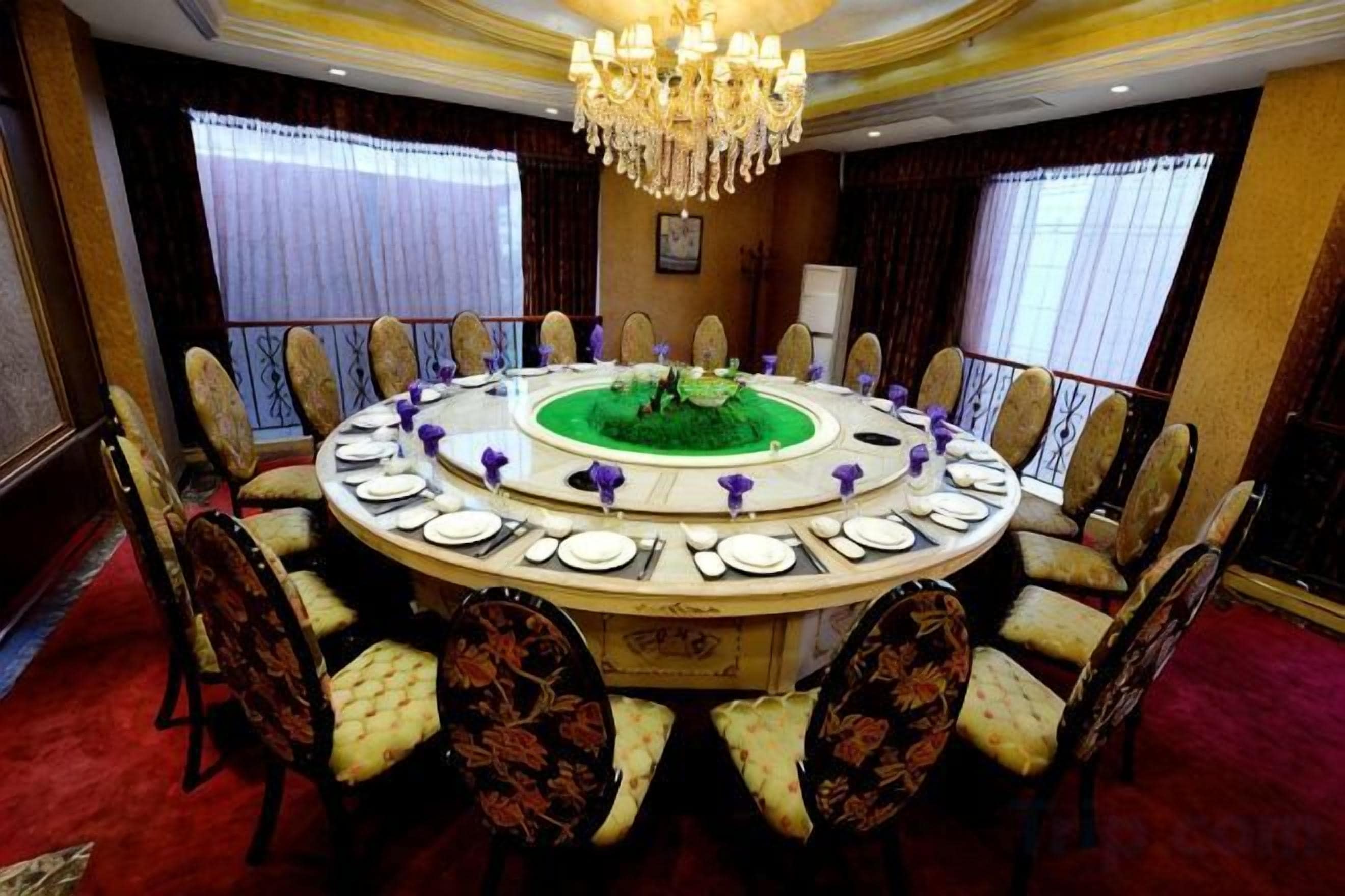 A round table with chairs, a chandelier, and a red carpeted floor.