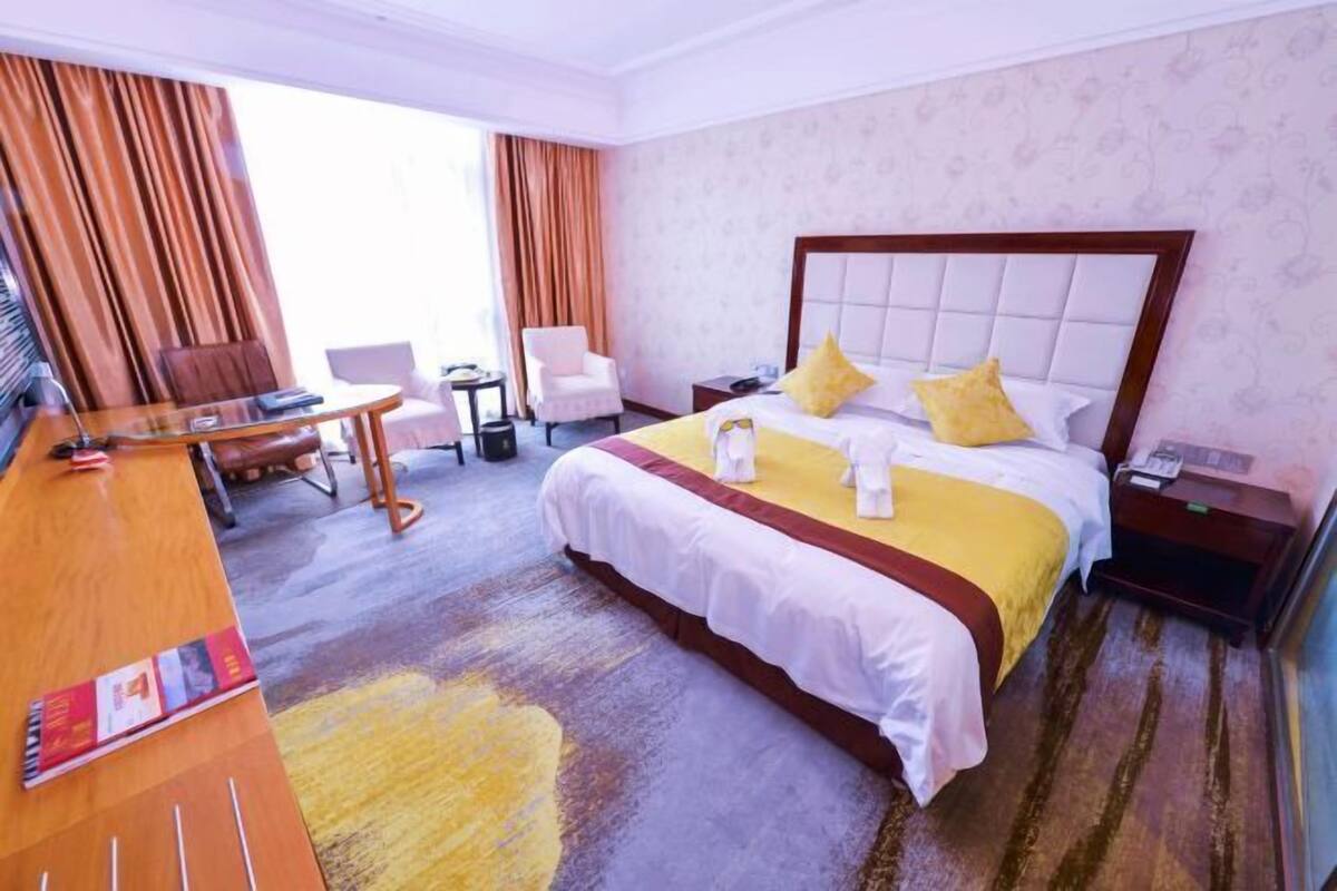 A hotel room with a large bed, a desk, a chair, and a small table.