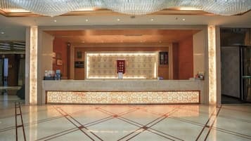 A hotel reception area with a reception desk, a decorative ceiling, and a tiled floor.