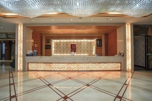A hotel reception area with a reception desk, a decorative ceiling, and a tiled floor. - Garden Hotel (Yilong)