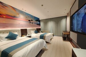 Habitación de hotel con dos camas, un cuadro grande de un atardecer, televisión y vista al mar desde la ventana.