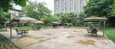 An outdoor patio area with brick flooring, tables, chairs, and umbrellas.