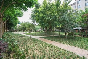 A landscaped garden with pathways, trees, and a building in the background. - Garden Hotel (Yilong)