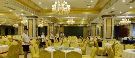 A banquet hall with round tables, chairs, and a stage.