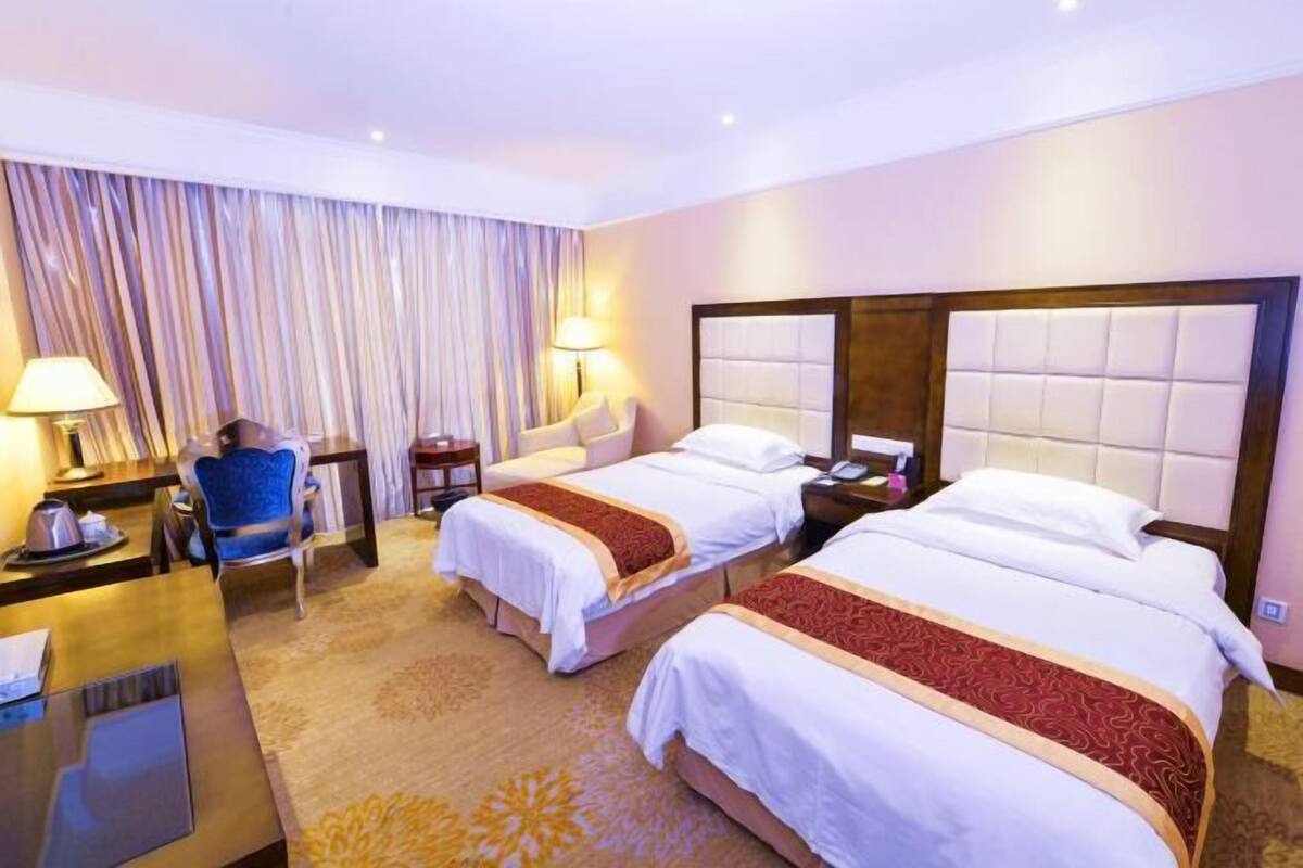 A hotel room with two beds, a desk, a chair, and a large window with curtains.