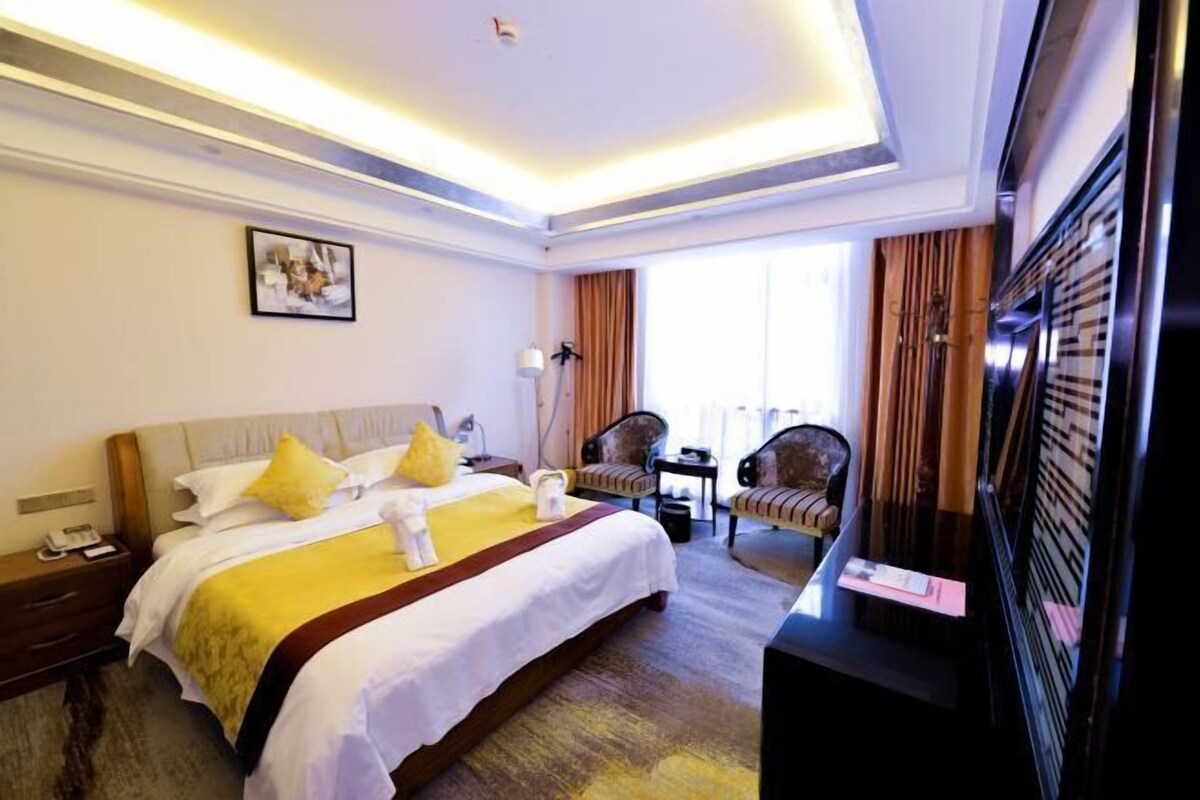 A hotel room with a large bed, a desk, a chair, and a television.