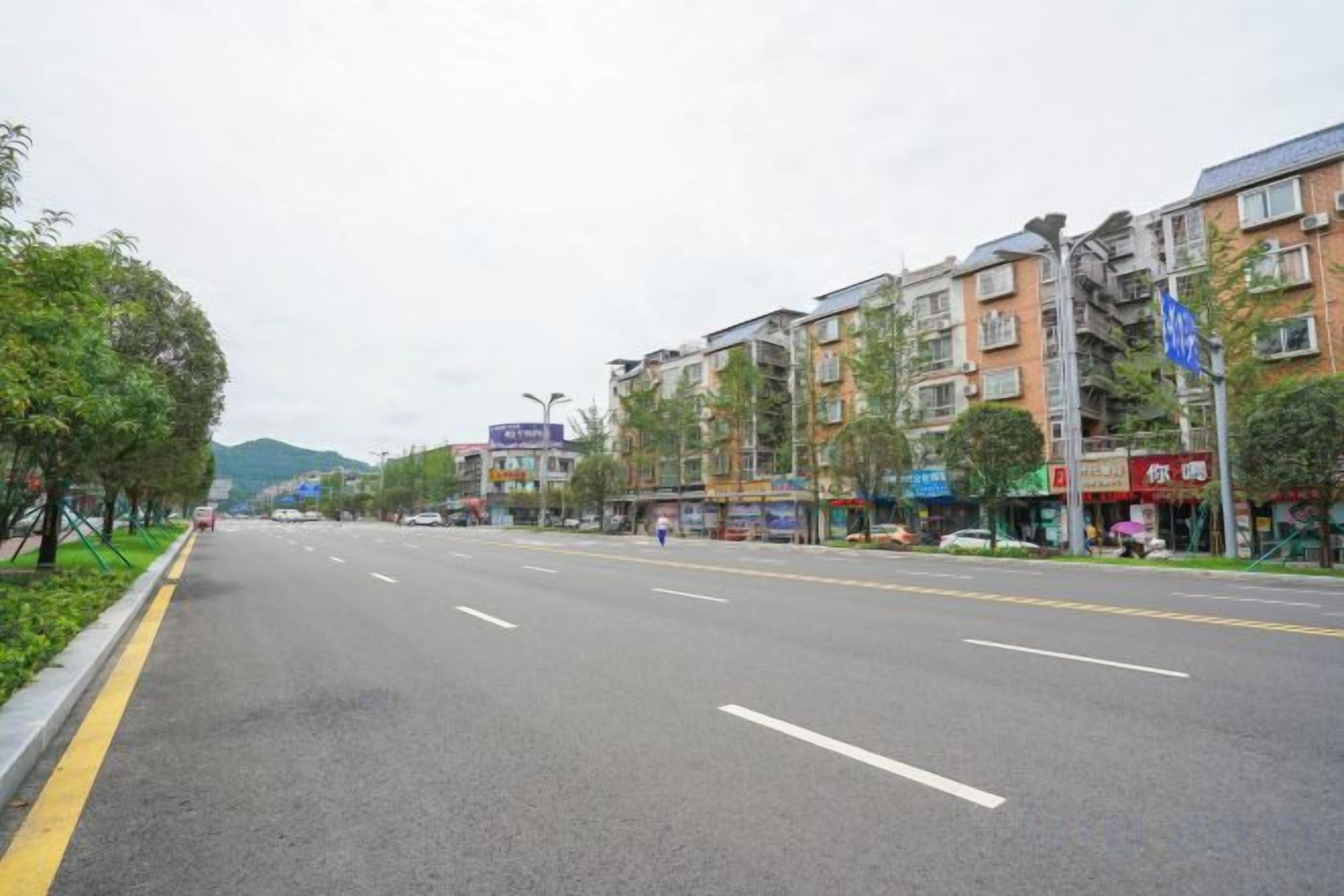 A wide, multi-lane road with buildings on both sides, including shops and residential units.