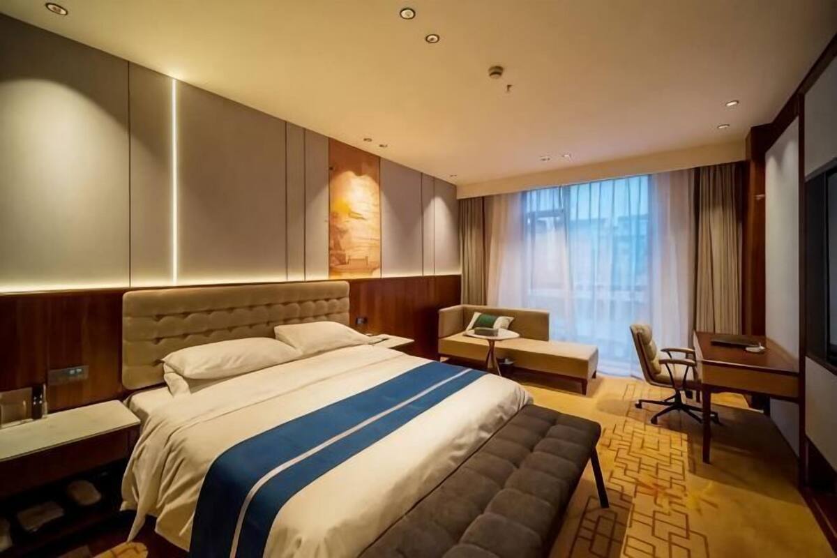 A hotel room with a large bed, a desk, a chair, and a TV.