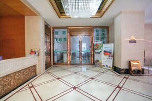 A hotel lobby with a reception desk, a check-in counter, and a glass door entrance. - Garden Hotel (Yilong)