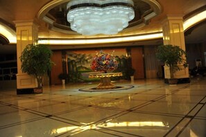 A lobby with a chandelier, a floral centerpiece, and potted plants. - Garden Hotel (Yilong)