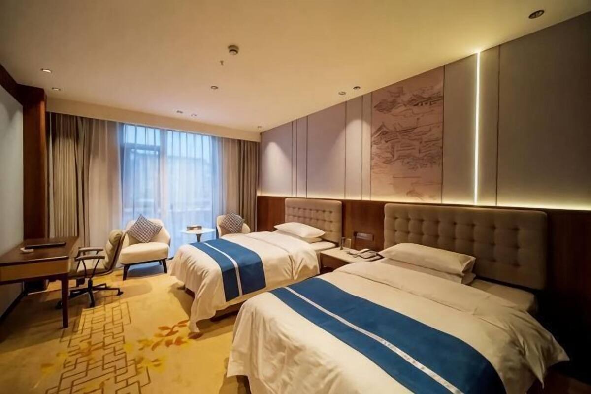 A hotel room with two beds, a desk, a chair, and a large window.