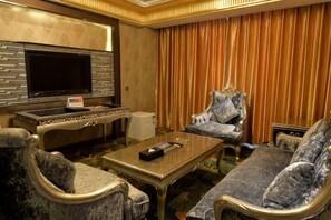 A living room with a flat-screen TV, a sofa, armchairs, a coffee table, and a large window with curtains. - Garden Hotel (Yilong)