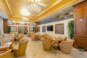 A spacious indoor area with multiple seating arrangements, including sofas and chairs, and a television mounted on the wall. - Garden Hotel (Yilong)
