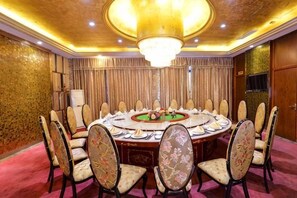 A round dining table with chairs, a chandelier, and a red carpet. - Garden Hotel (Yilong)