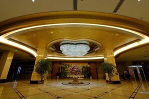 A spacious lobby with a large chandelier, two potted plants, and a central decorative piece.