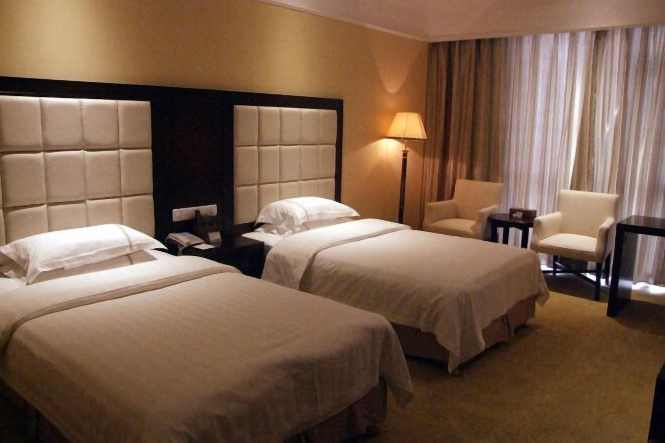 Quarto de hotel com duas camas, uma cadeira, um abajur e uma pequena mesa.