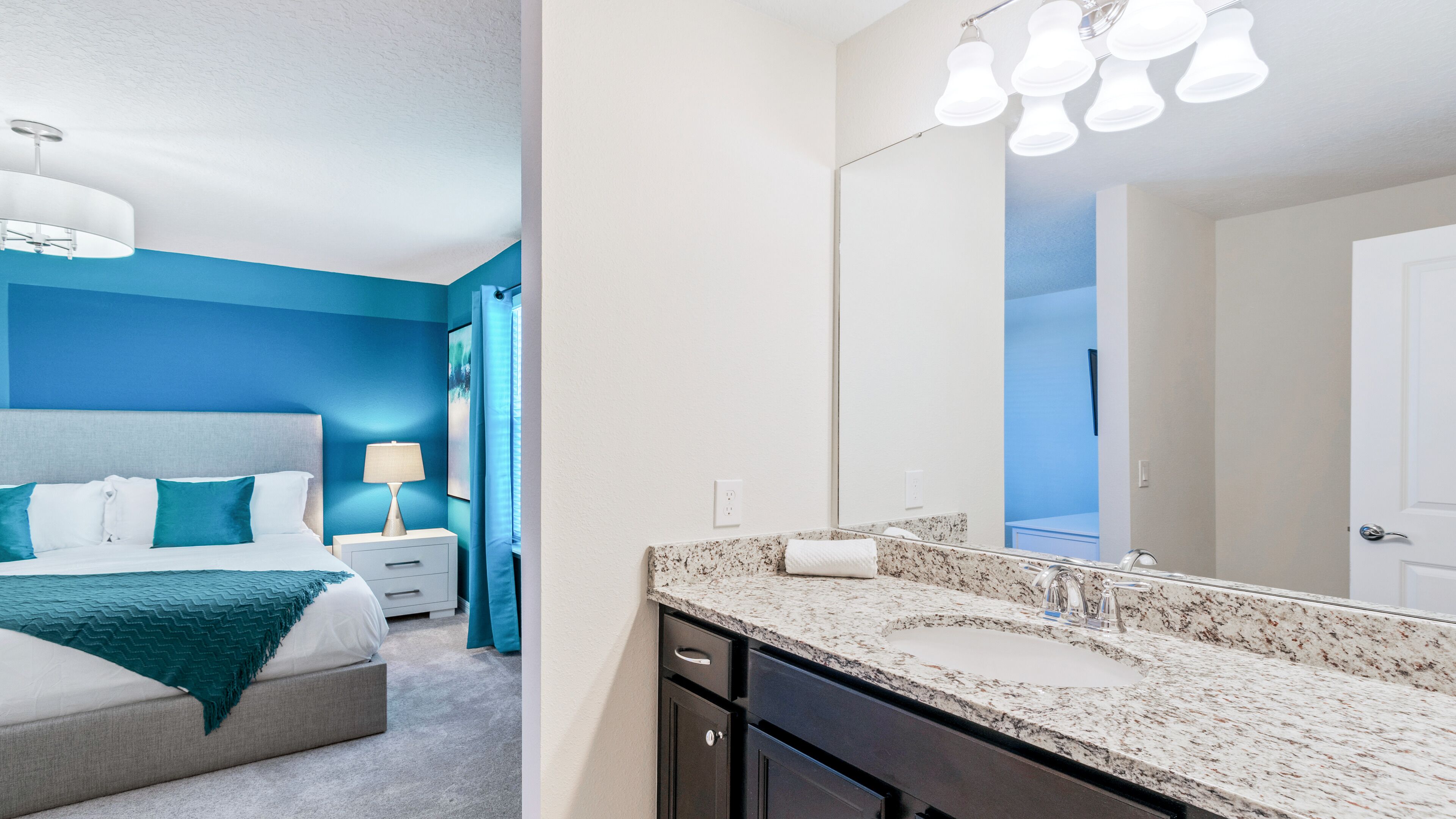 A hotel room with a bed, nightstand, lamp, and a bathroom with a sink and mirror.