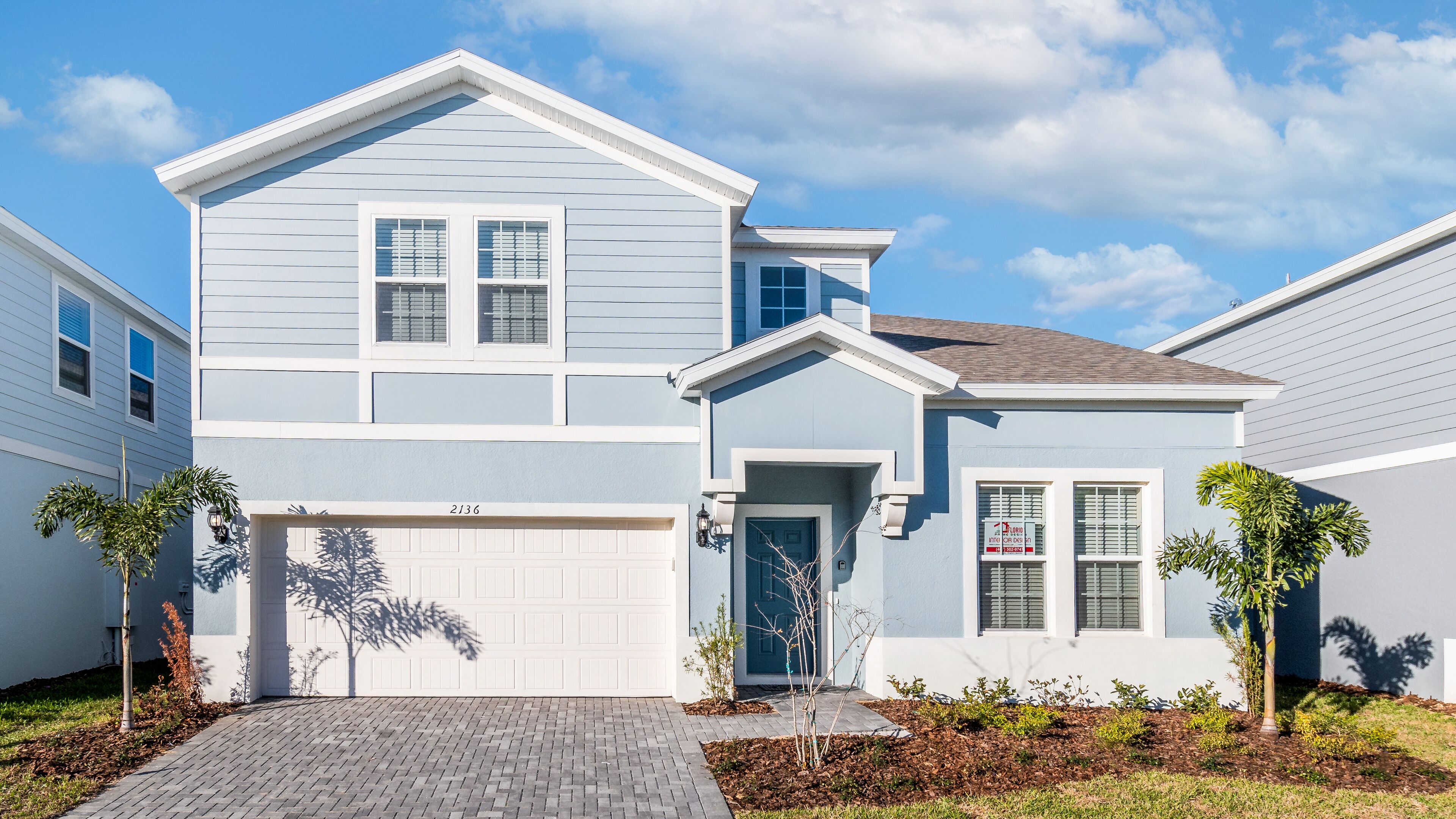A two-story house with a garage, a front door, and a small front yard with plants.