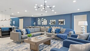 Un salon moderne avec un canapé d’angle, une table basse et un coin repas, la cuisine étant visible au fond.