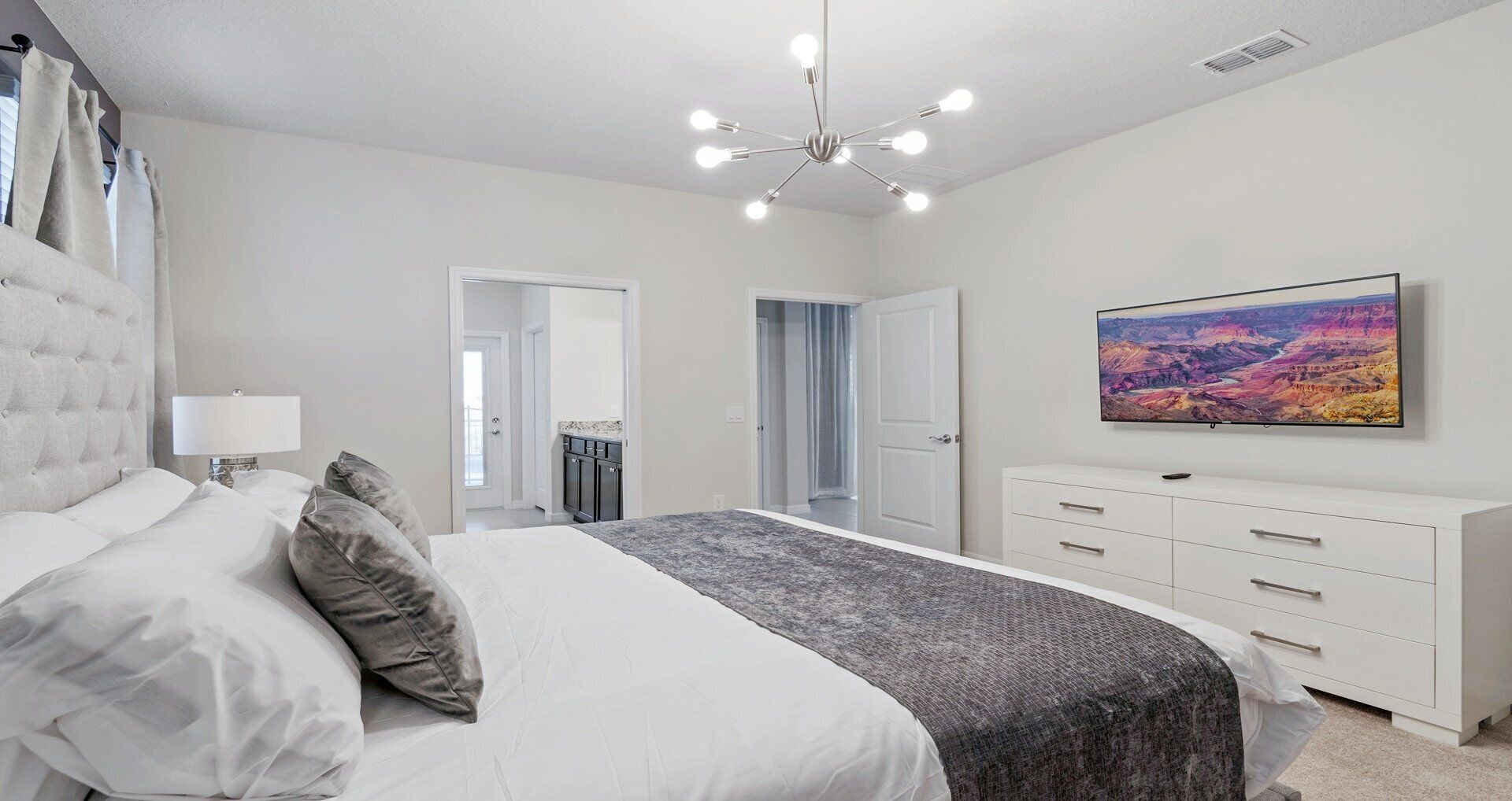 A bedroom with a bed, a dresser, a TV, and a chandelier.