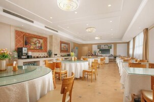 Un comedor de hotel con mesas redondas, sillas y una cocina al fondo.