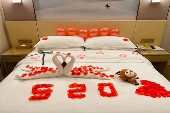 Une chambre d’hôtel avec un lit décoré de pétales de rose et un arrangement en forme de cygne, un jouet en peluche, et le chiffre « 520 » épelé avec des pétales.
