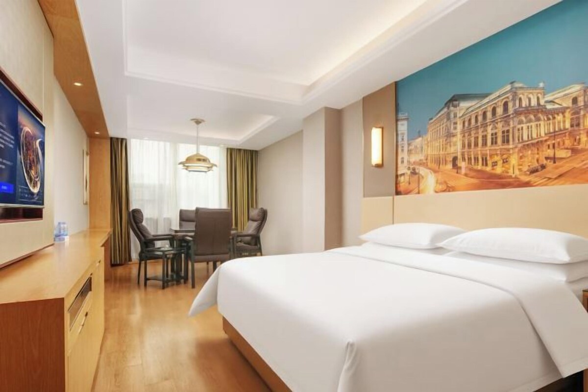 Ein Hotelzimmer mit Bett, Schreibtisch, Stuhl, Fernseher und einem Bild an der Wand.