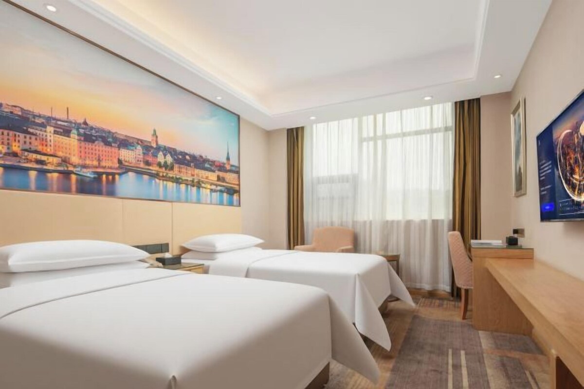 Ein Hotelzimmer mit zwei Betten, einem Schreibtisch und einem großen Fenster.