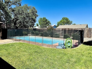 A backyard with a swimming pool, a fenced area, and a grassy lawn.
