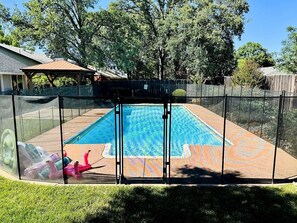 A backyard with a swimming pool, surrounded by a fence, and trees in the background.