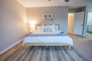 A bedroom with a bed, bedside tables, a nightstand, a lamp, and a door.